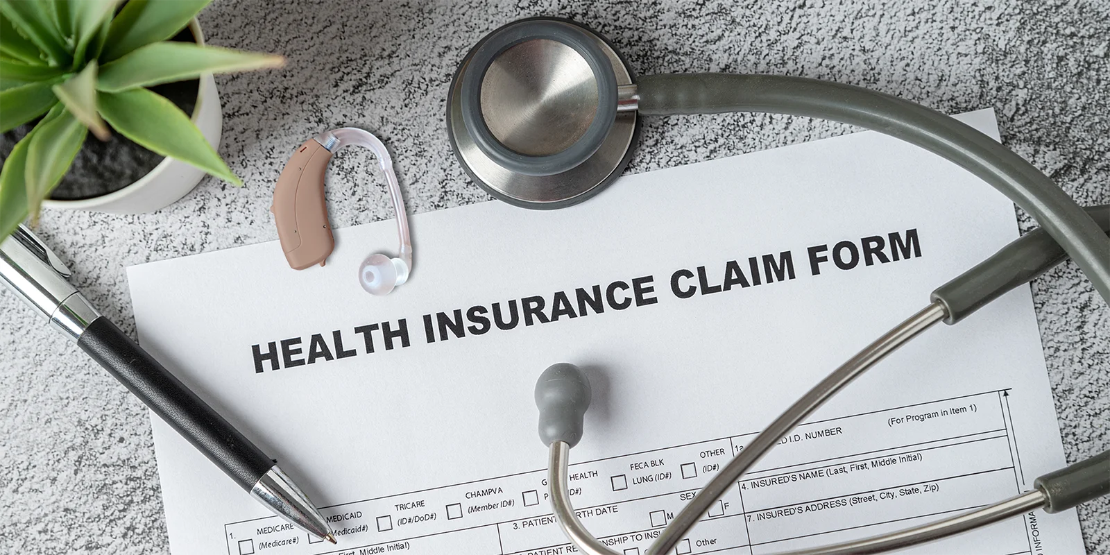 health insurance claim form on desk with stethoscope, hearing aid, and pen