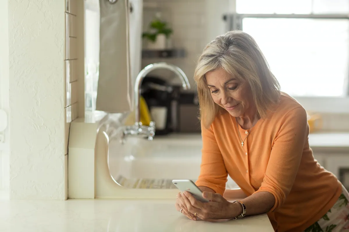 Woman using mobile phone standing in kitchen