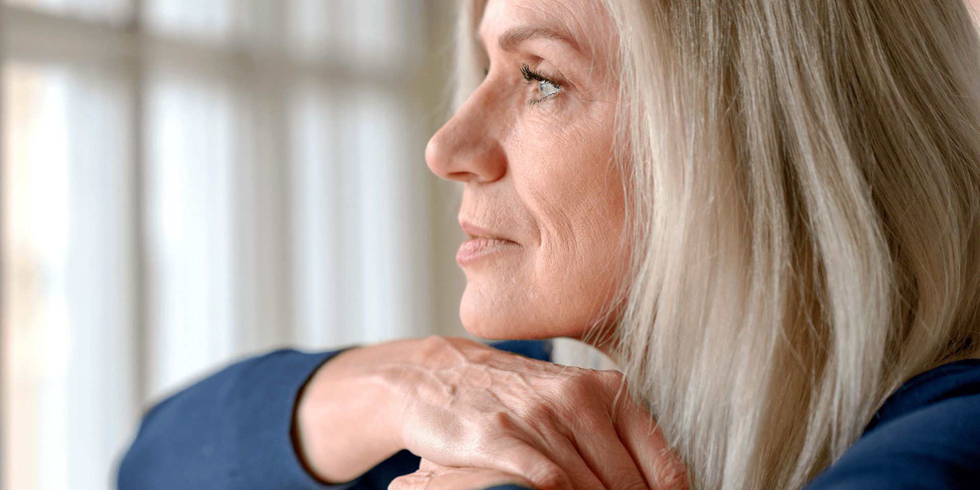 Woman with untreated hearing loss wearing a blue shirt and looking out a window